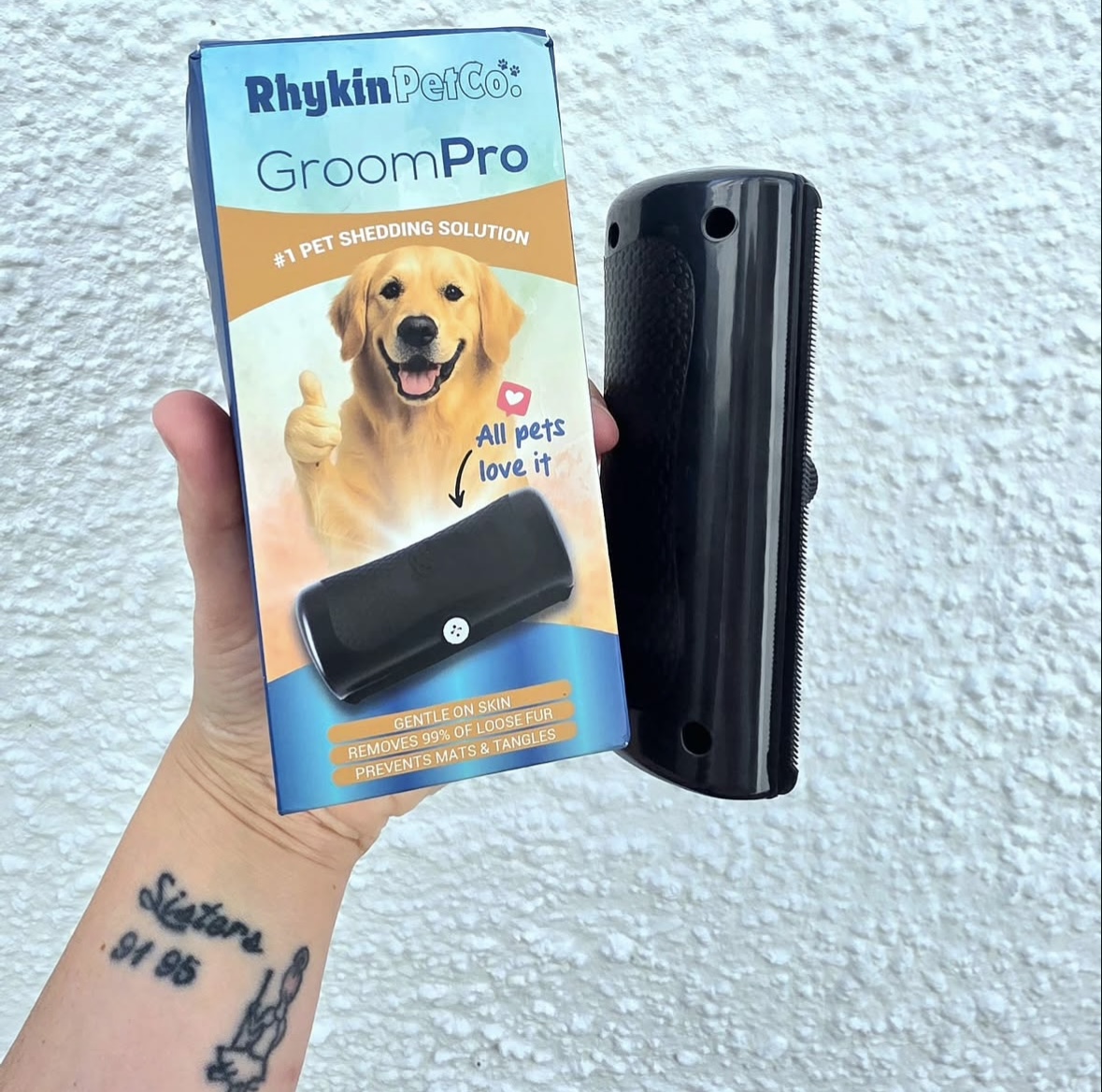 Hand holding a pet grooming tool and its packaging against a textured wall.