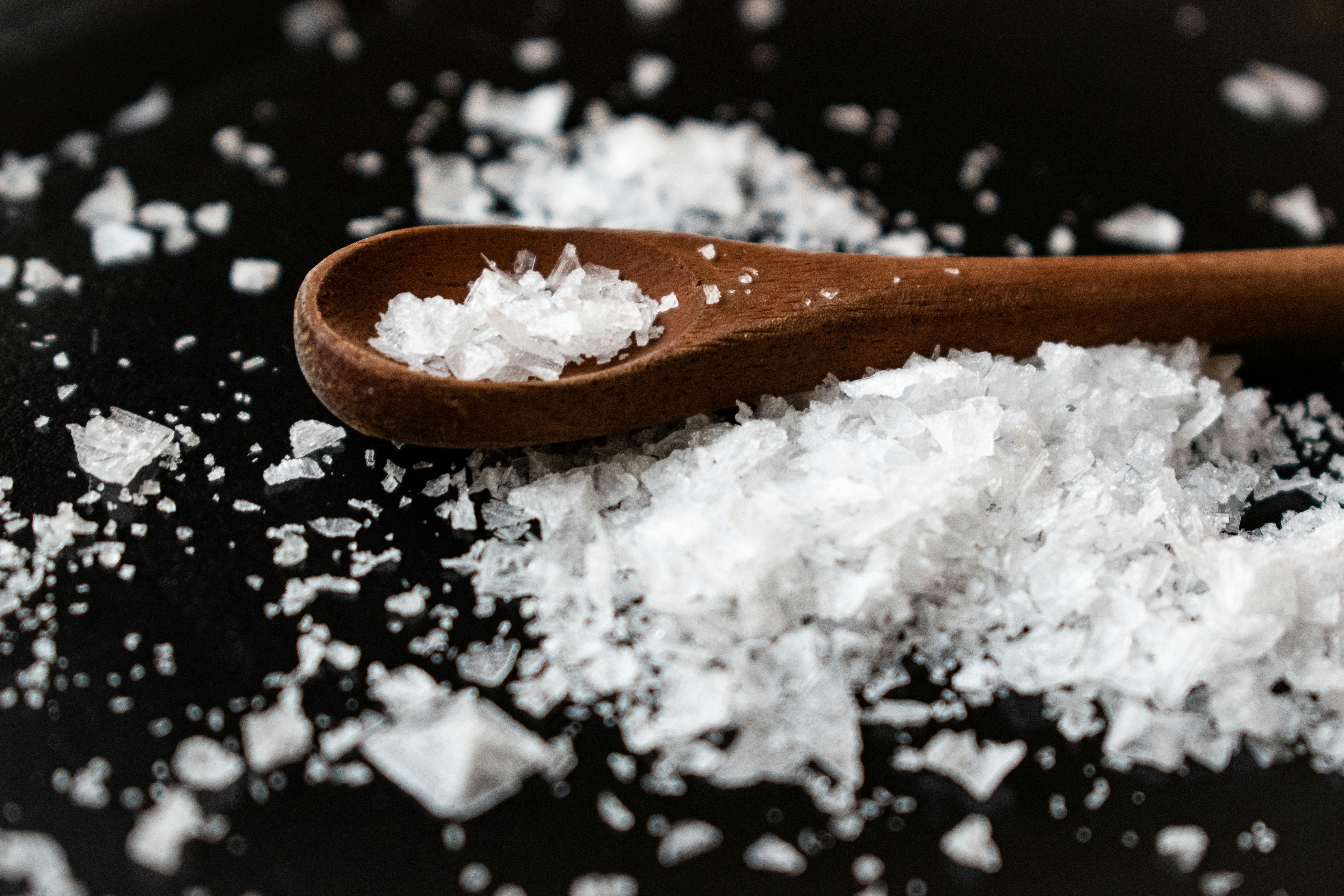 Wooden spoon with coarse salt on a dark surface.