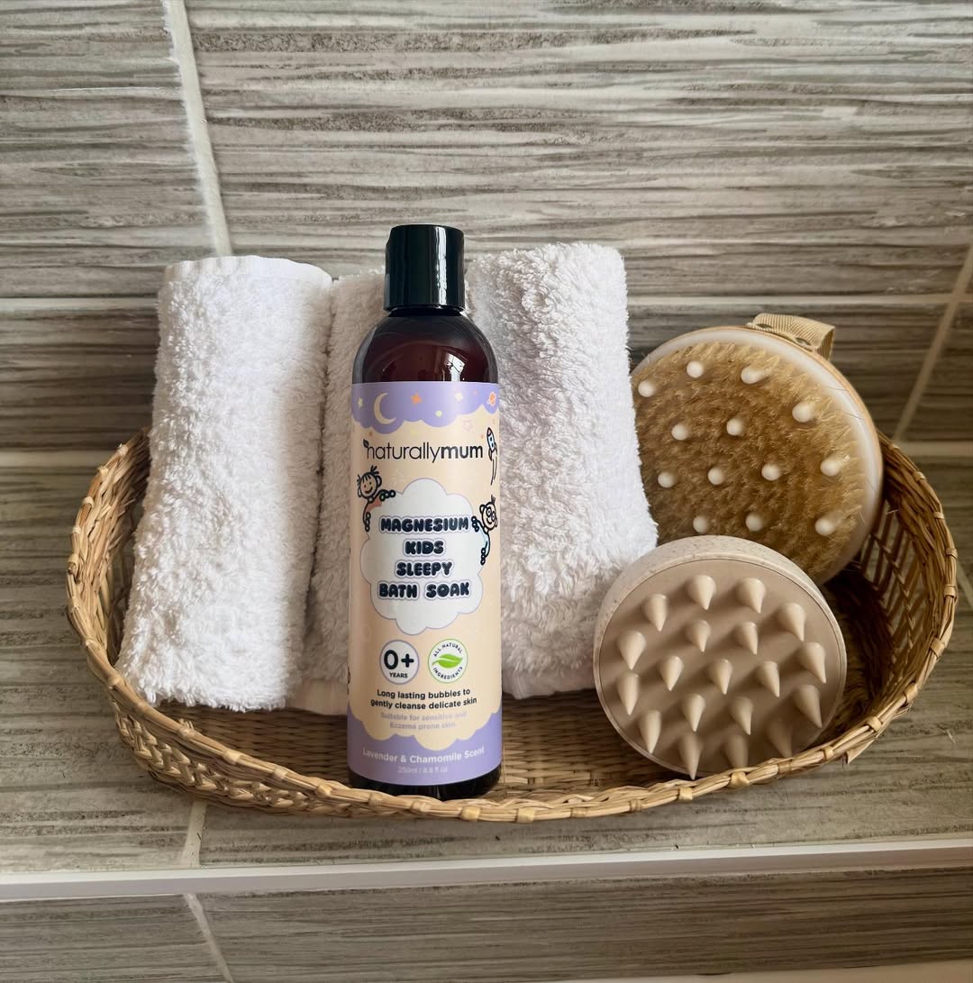 Basket with bath soak, towels, and brushes on a tiled surface.
