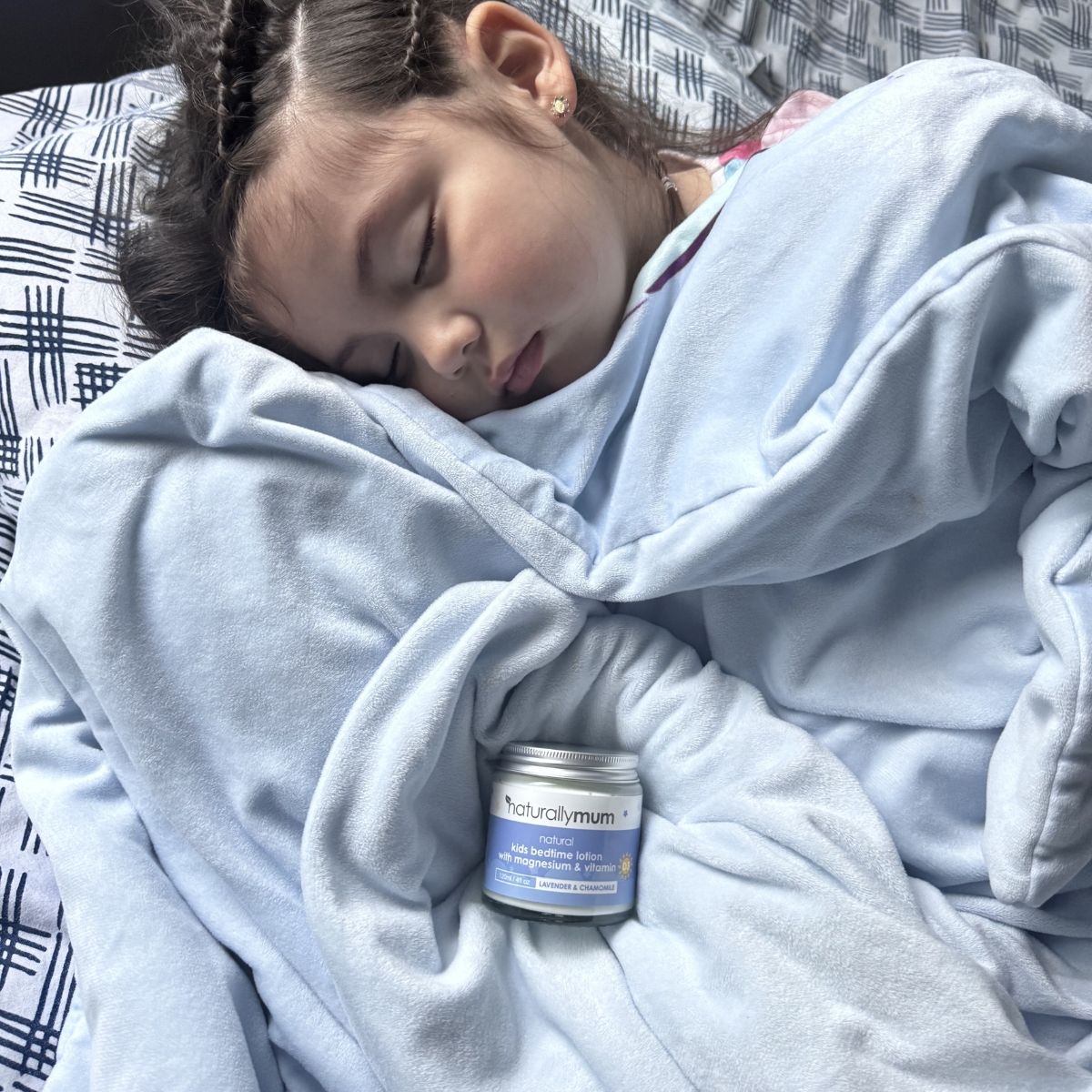 A mother holds her sleeping daughter in bed, who is cuddling a stuffed bunny.