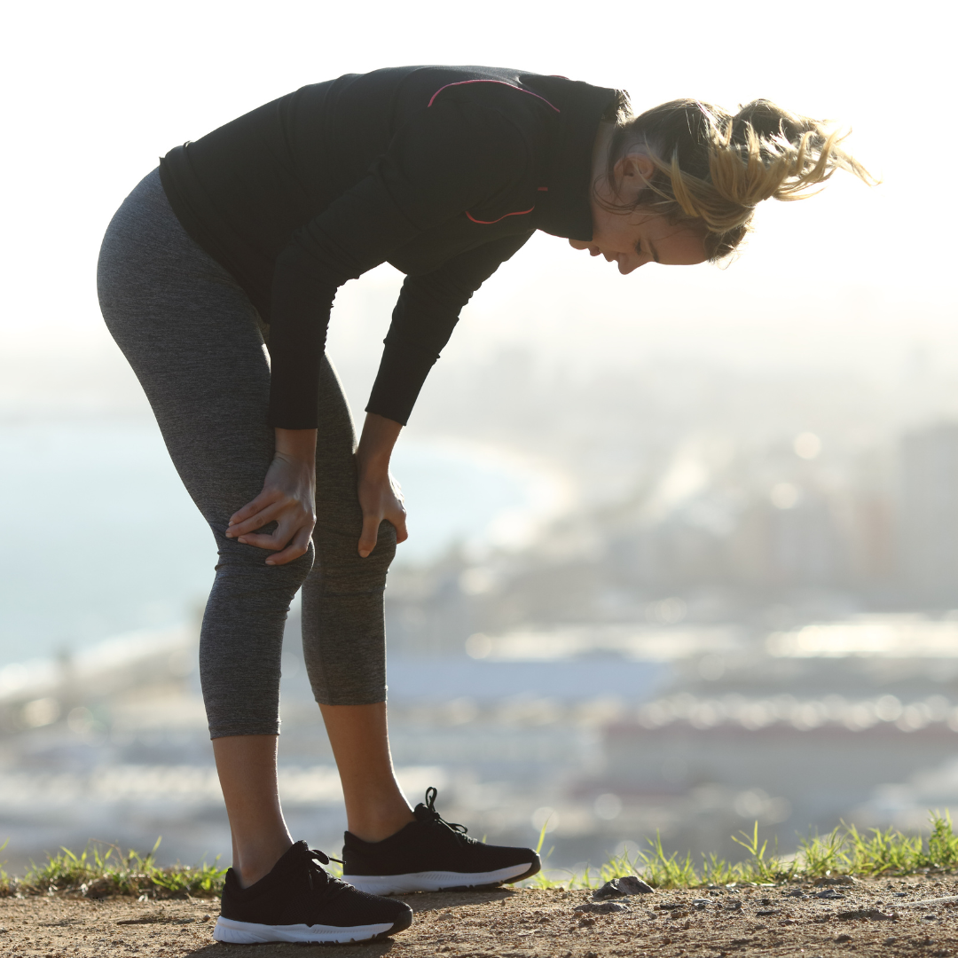 Person bending over, resting on a hilltop with a blurred cityscape in the background.