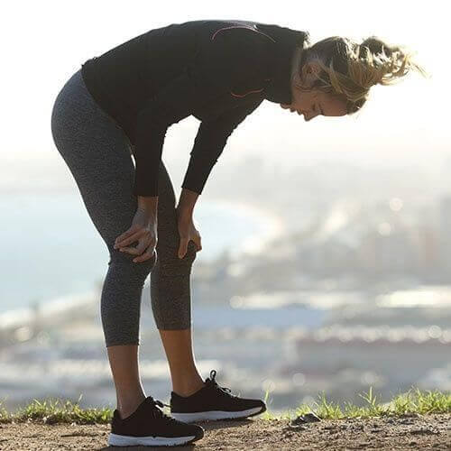 Woman in athletic wear resting on a hill with a cityscape in the background.