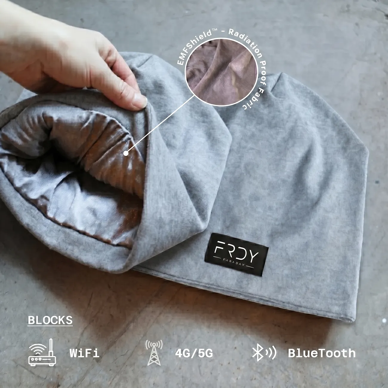 A hand holds open a grey beanie, showing its shiny, silver, radiation-proof inner lining.