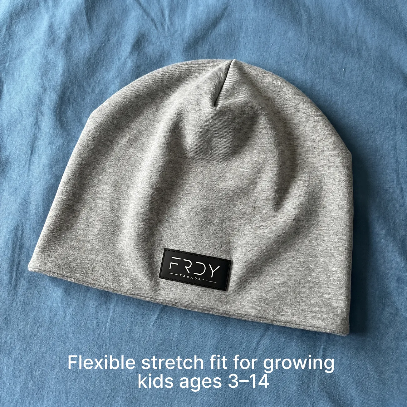 A gray heather beanie with a black FRDY Faraday logo patch, lying on a blue fabric background.