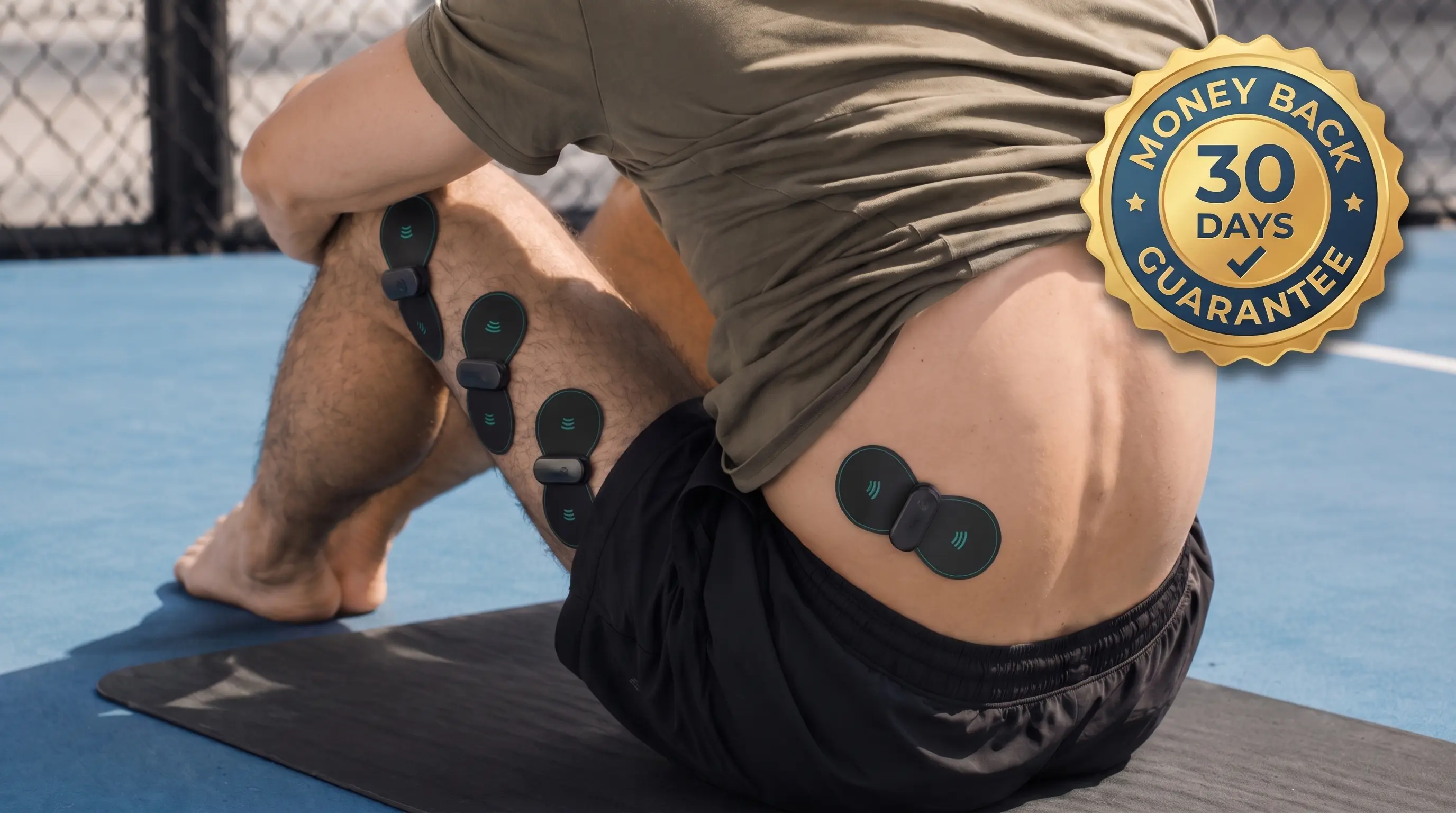 A man sits on a mat with electronic muscle stimulator pads on his leg and lower back.