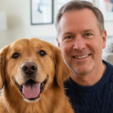 A smiling, middle-aged man with short brown hair sits next to a golden retriever.