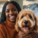 A smiling woman with braids in a rust-colored sweater holds a fluffy, light-brown dog.