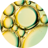A circular, close-up photograph of yellowish-green oil bubbles suspended in a liquid.