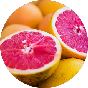 A circular close-up photo of a vibrant pink grapefruit sliced in half, resting among other whole grapefruits.