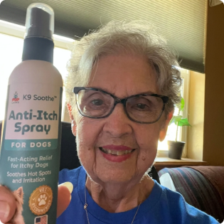 A smiling woman holds up a bottle of K9 Soothe Anti-Itch Spray for dogs.