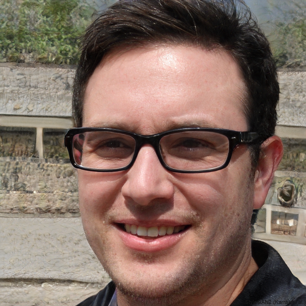 A close-up photograph of a smiling man with dark hair and black-rimmed glasses.