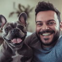 A smiling man with a beard poses for a photo next to a happy grey French Bulldog.