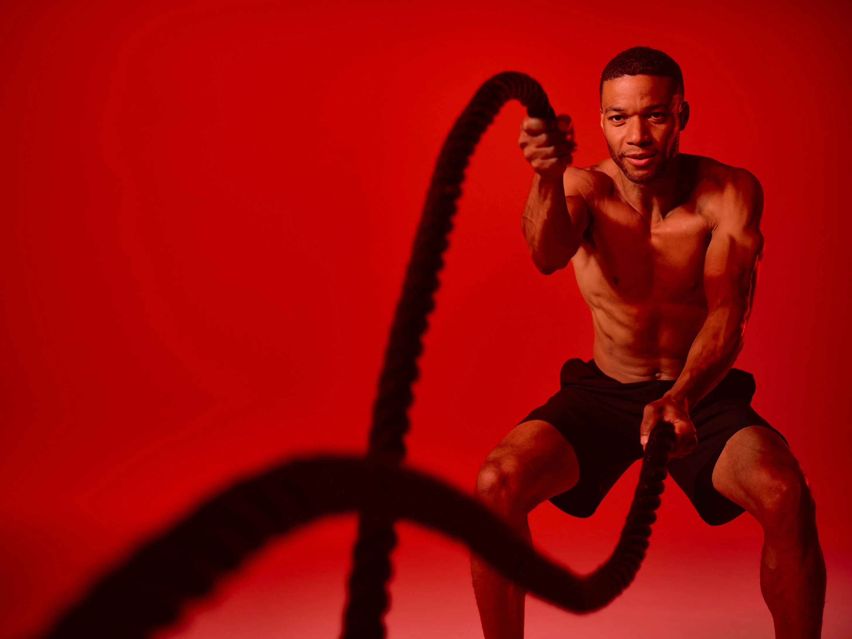 Man exercising with battle ropes against a red background.
