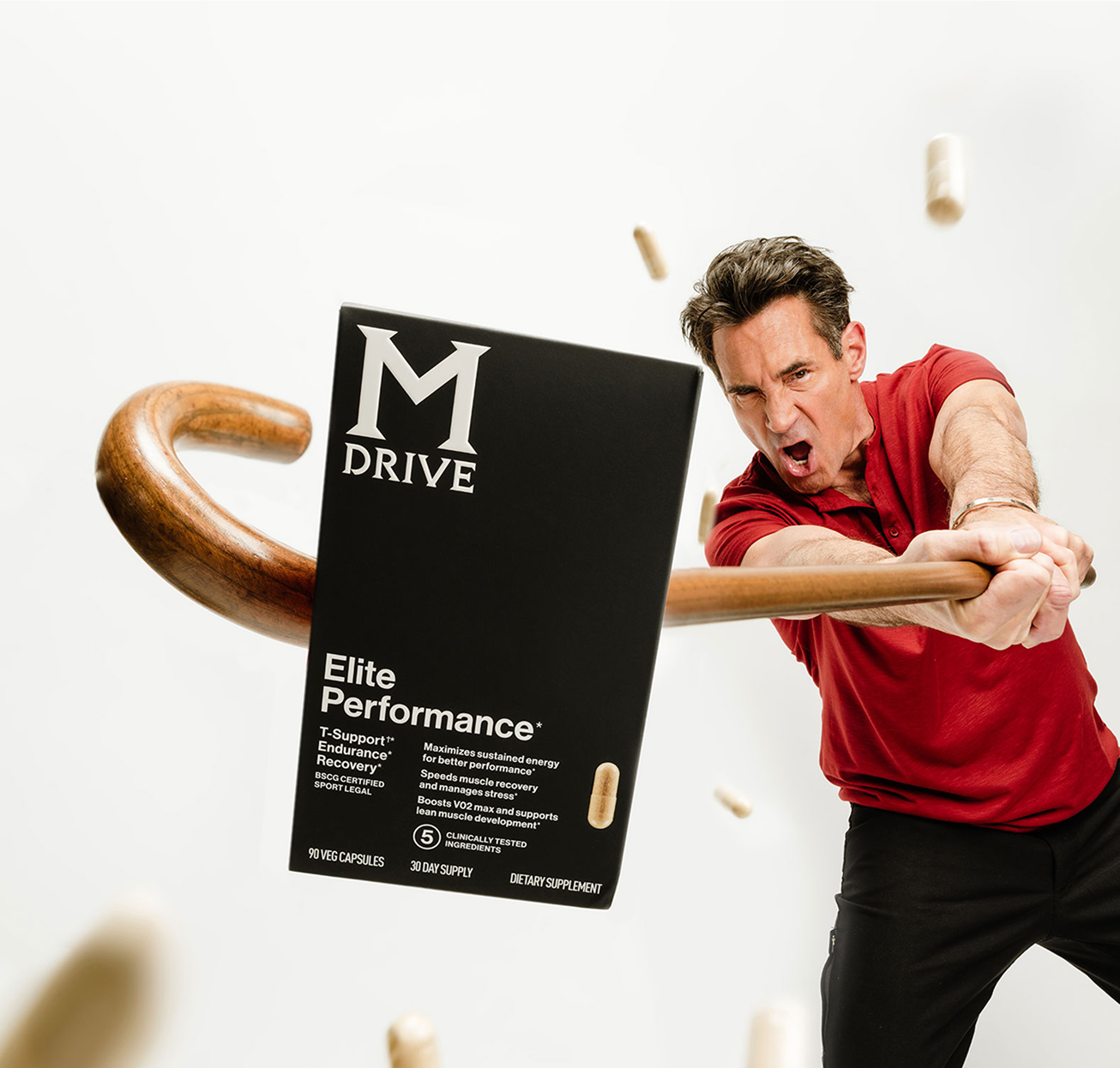 Man in red shirt swinging a wooden bat at a black box labeled 'M Drive Elite Performance.'