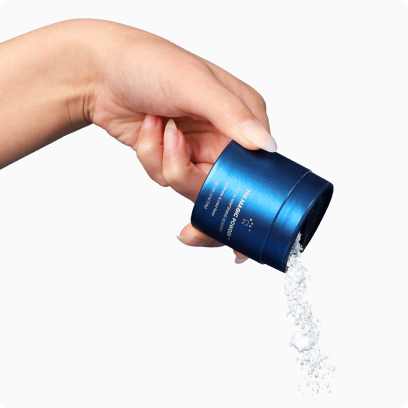 Hand pouring powder from a blue container against a white background.