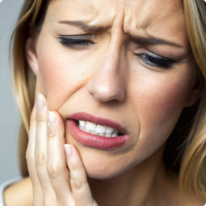 Woman wincing in pain, holding her cheek, indicating a toothache.