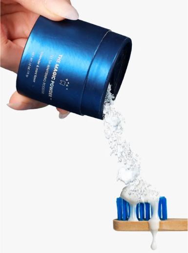 Pouring tooth powder onto a toothbrush from a blue container.