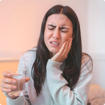 Woman holding jaw in pain, holding a glass of water.