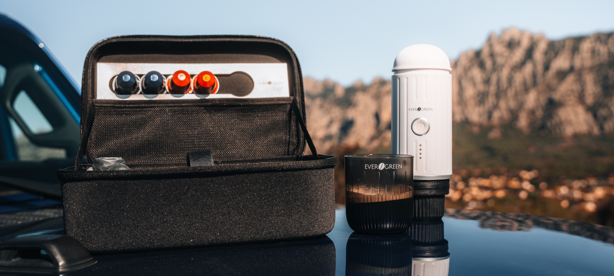 Portable coffee maker and capsules on a car with mountains in the background.