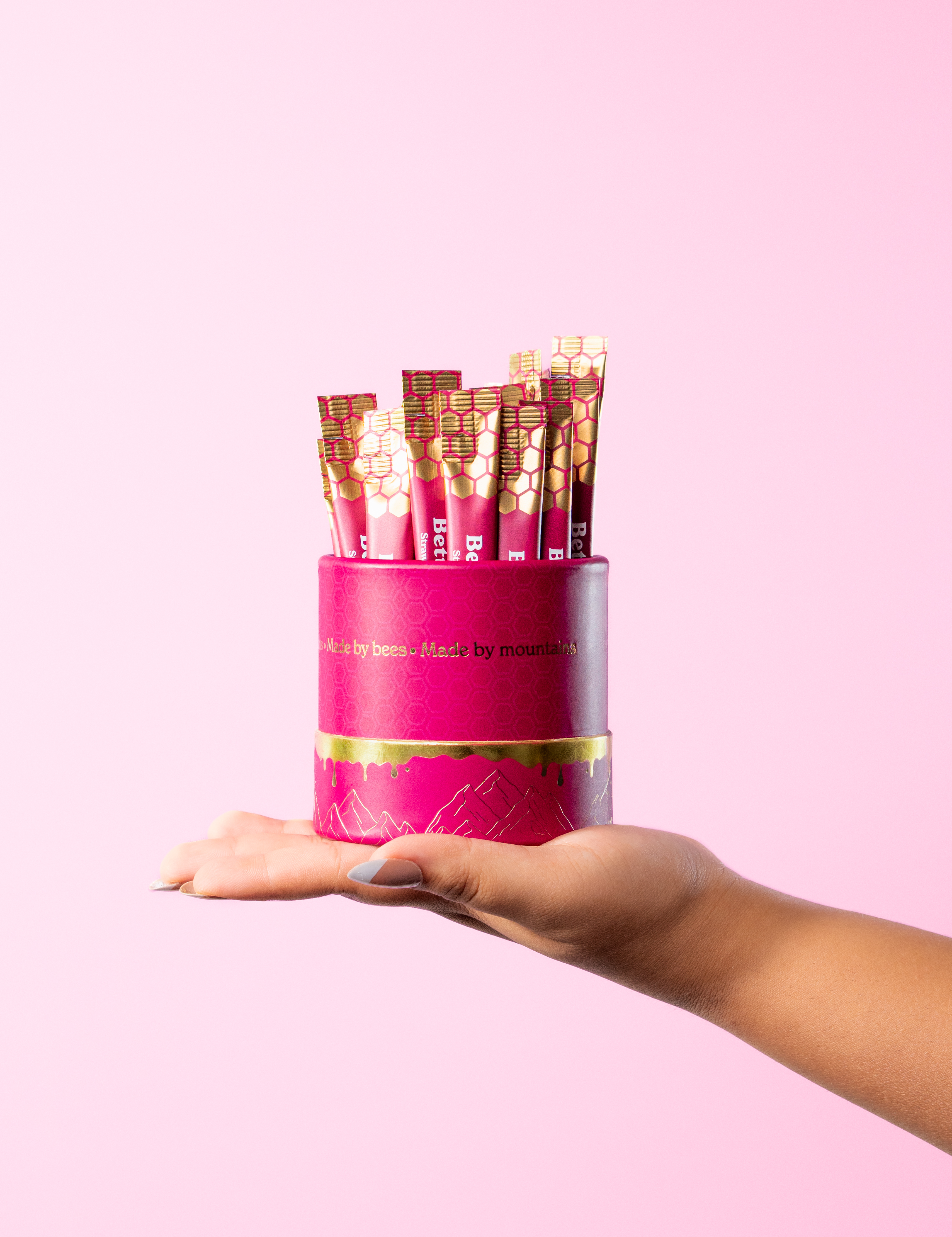 Hand holding a pink container with honey packets against a pink background.