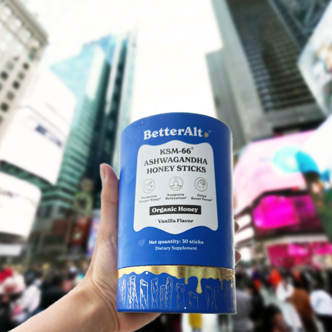 Hand holding a container of ashwagandha honey sticks in a cityscape background.