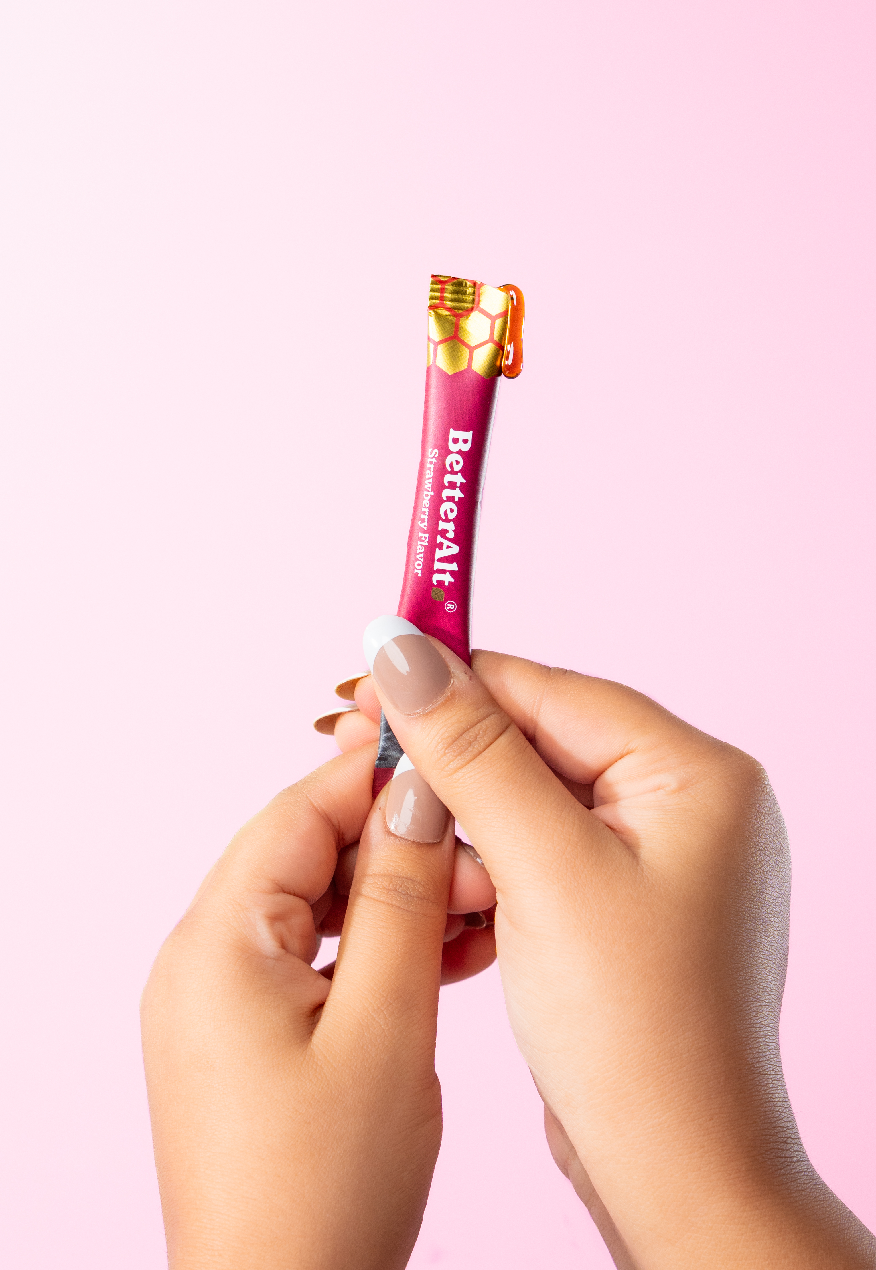 Two hands holding a small pink tube with gold honeycomb pattern on top.