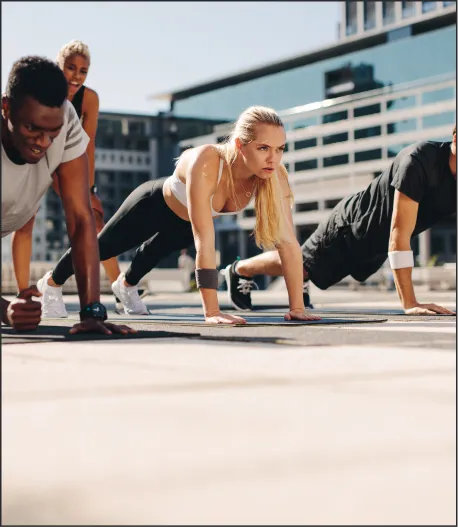 A group of people in a plank position, exercising together outdoors in an urban setting.