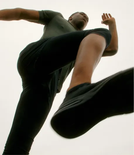 A low-angle shot of a man in dark athletic wear running against a plain background.