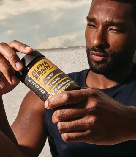 A man in a tank top holds a bottle of Onnit Alpha Brain supplements.