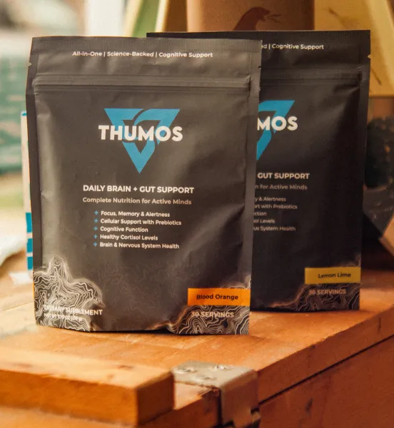 Two black pouches of Thumos Daily Brain + Gut Support supplement on a wooden surface.