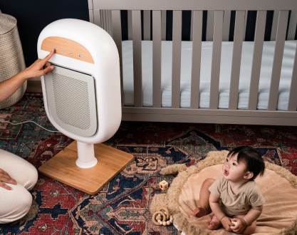 A person adjusts a floor-standing air purifier in a nursery while a baby sits on the rug.