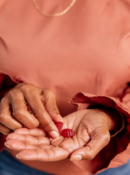 A person wearing a salmon-colored shirt holds red gummies in their hand.