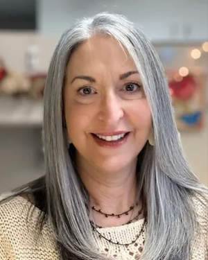 A headshot of a smiling woman with long, straight, gray hair looking at the camera.