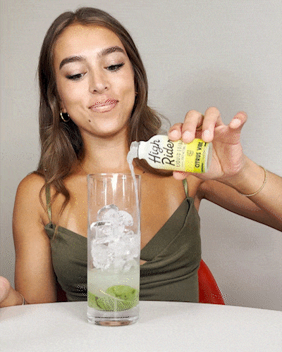 Person pouring liquid from a bottle into a glass with ice and lime.