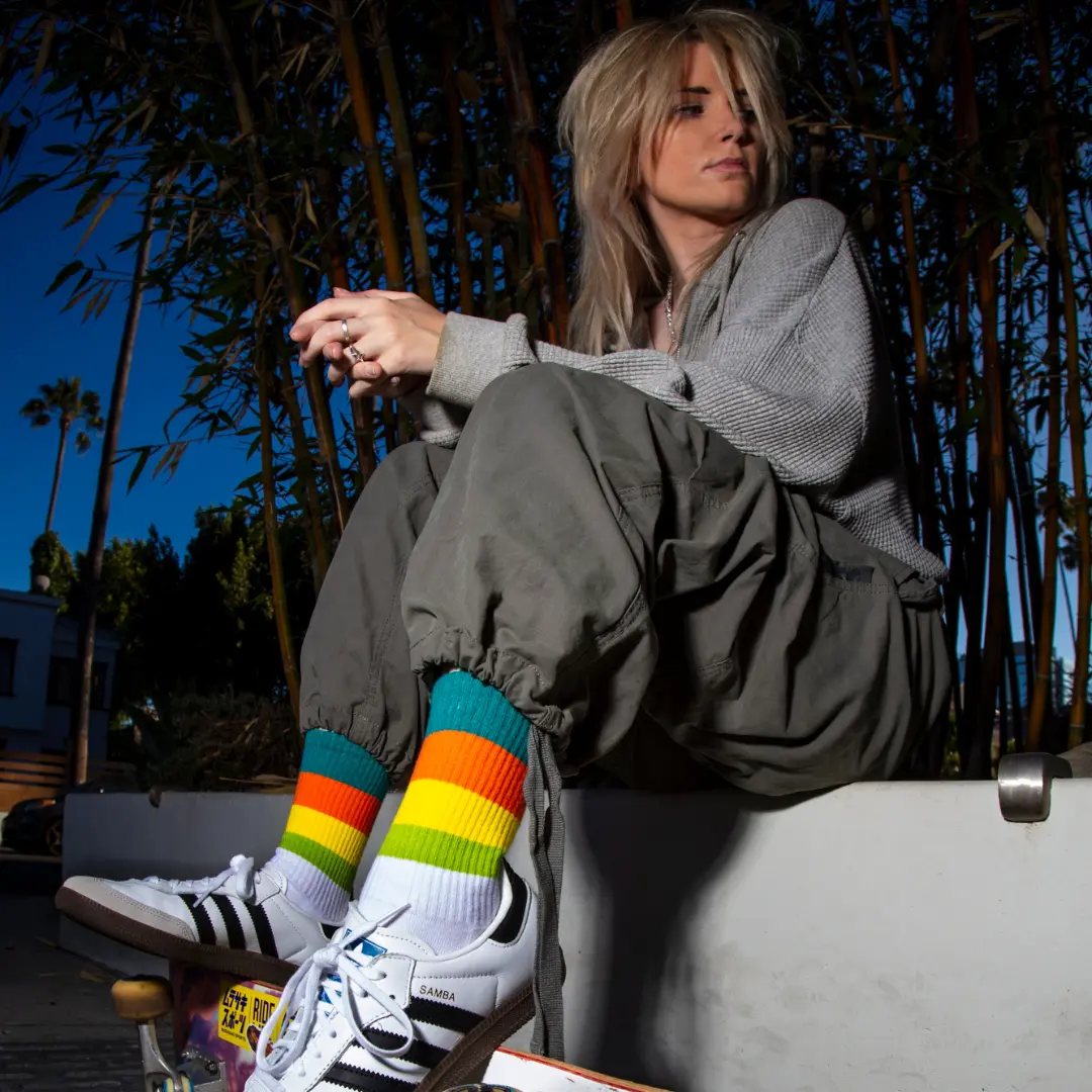 Person sitting outdoors wearing colorful striped socks and sneakers, surrounded by bamboo plants.