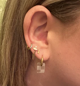 Close-up of an ear with multiple gold earrings and a transparent square drop.