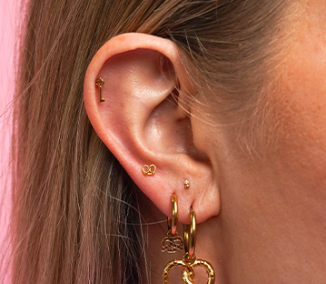 Close-up of an ear with multiple gold earrings, including a key-shaped stud.