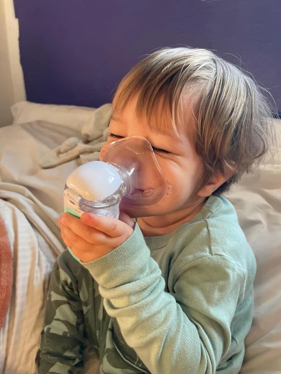 Child using a nebulizer, sitting on a bed.