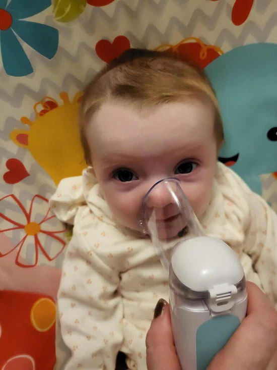 Baby receiving inhaler treatment on a colorful patterned background.