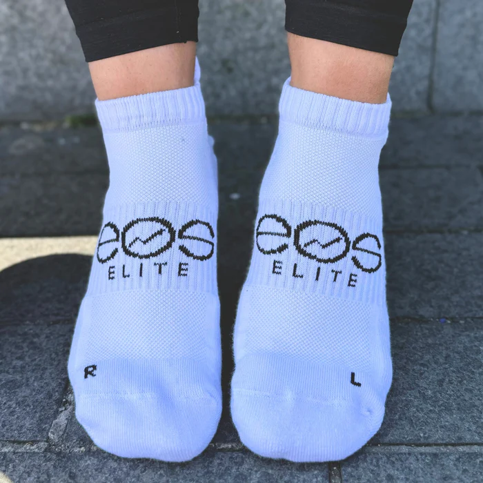 Person wearing white socks with 'eos ELITE' text on pavement.