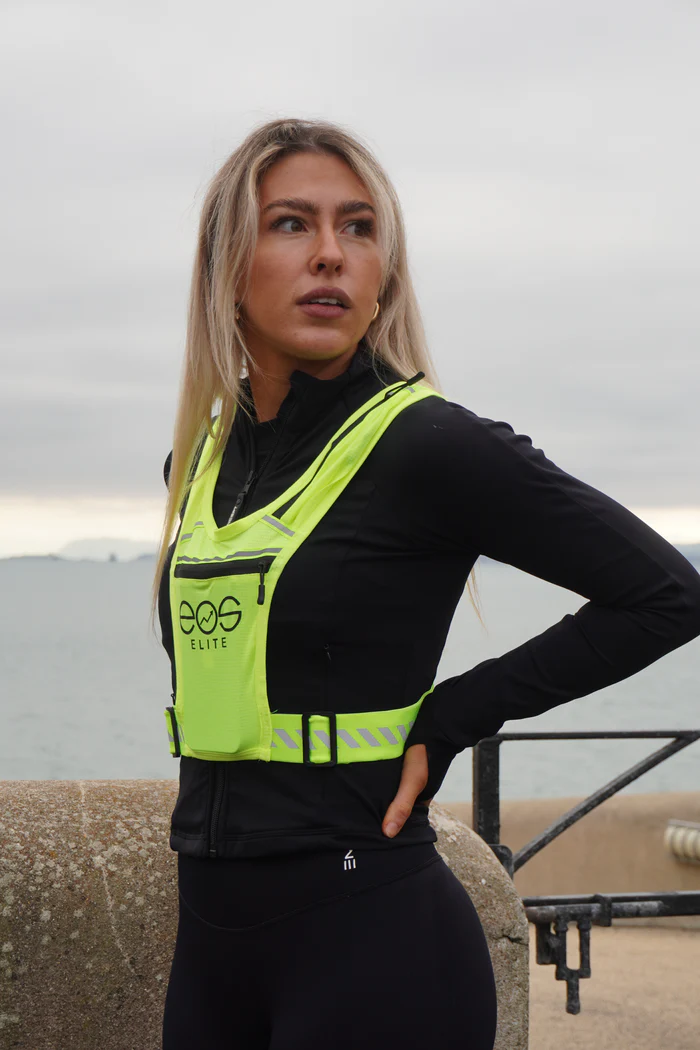 Person wearing a neon safety vest near a waterfront.