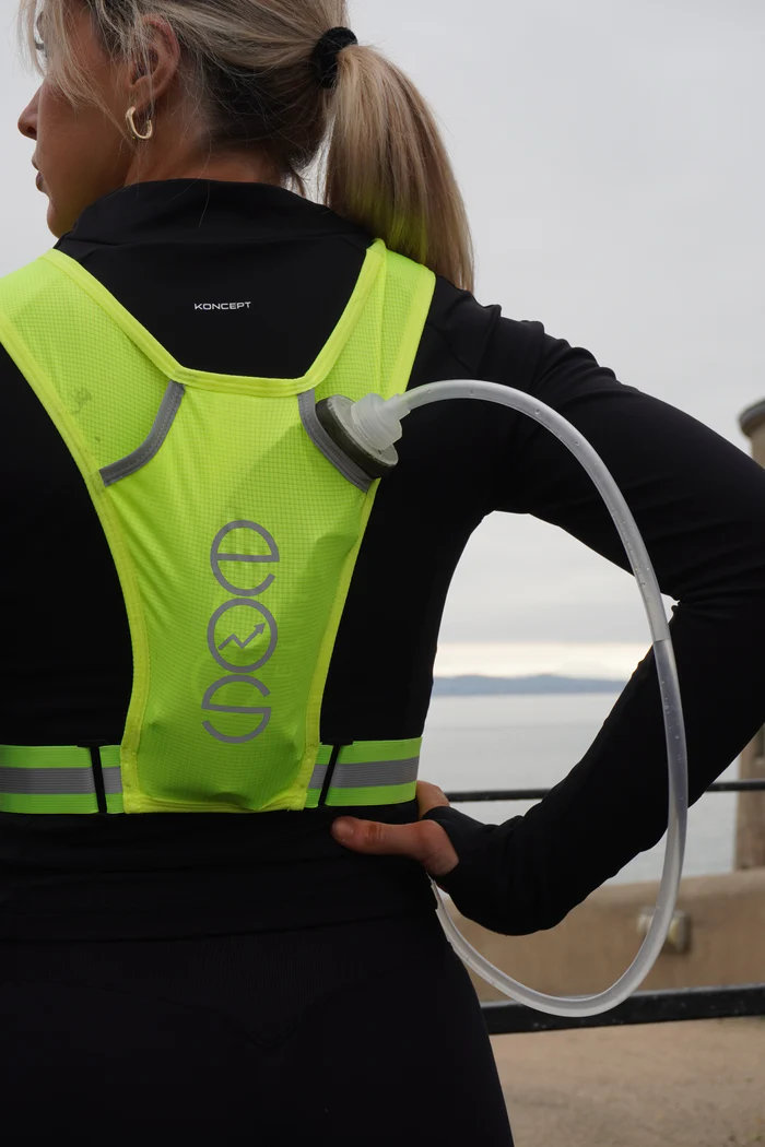 Person wearing a neon green hydration pack with a tube, standing outdoors.