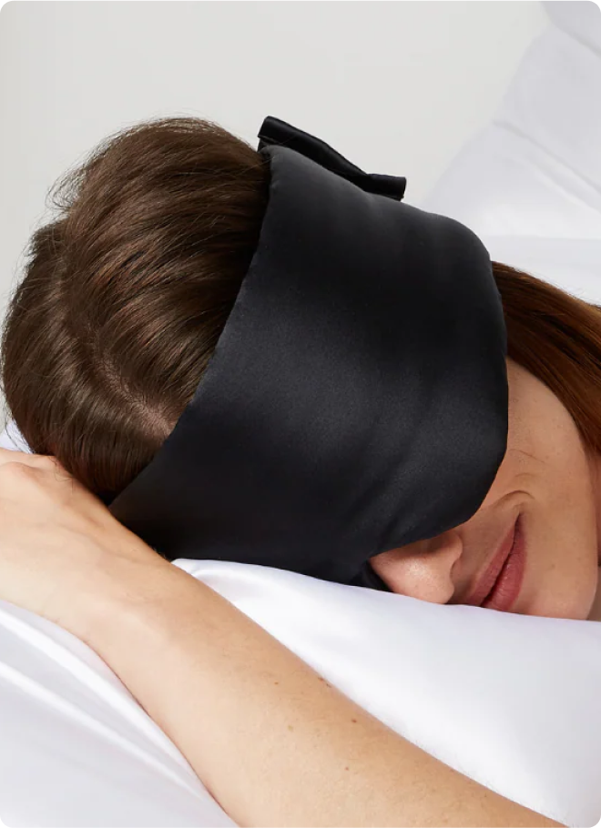 Person sleeping with a black sleep mask on a white pillow.