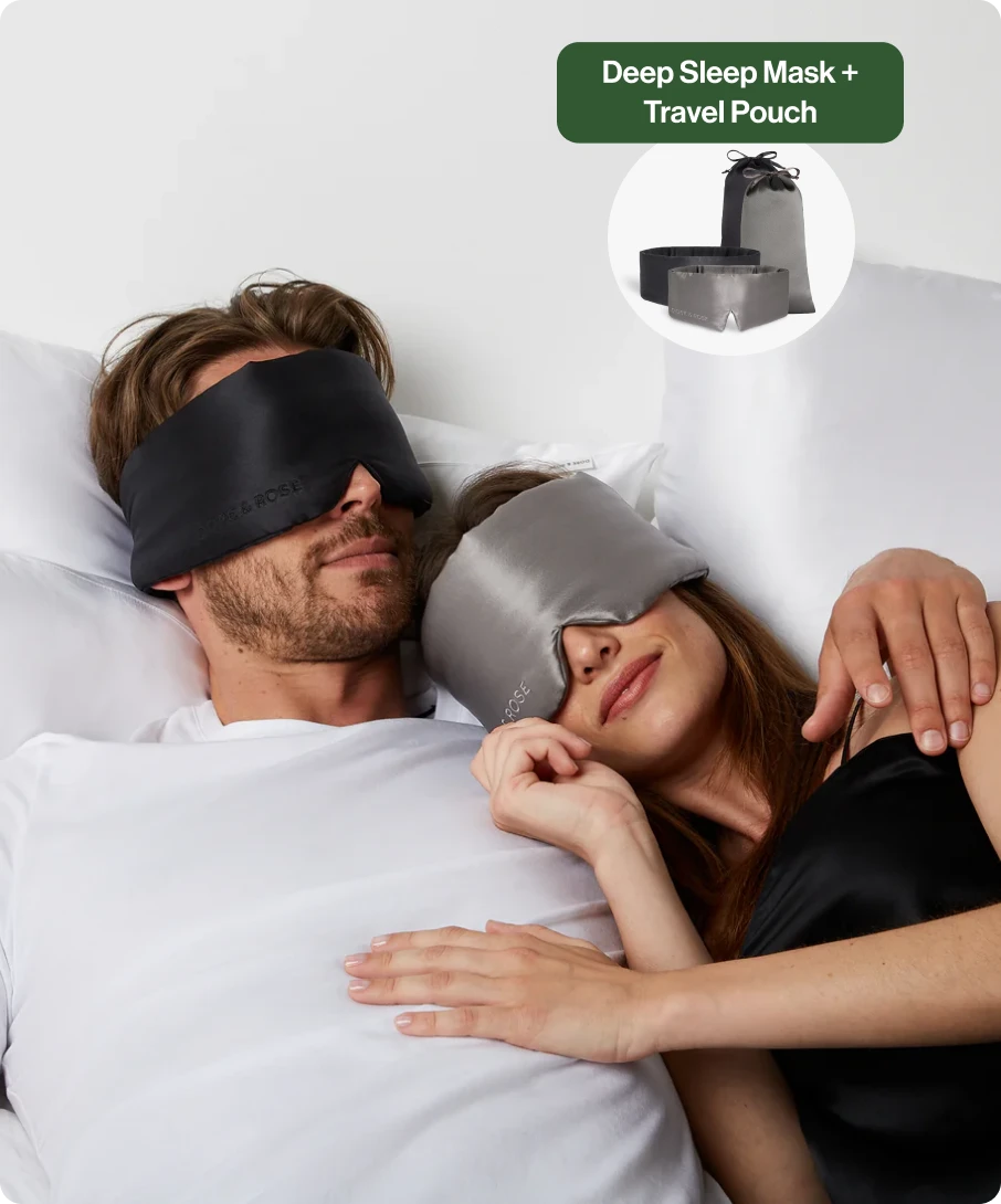 Couple wearing sleep masks, lying in bed with arms around each other.