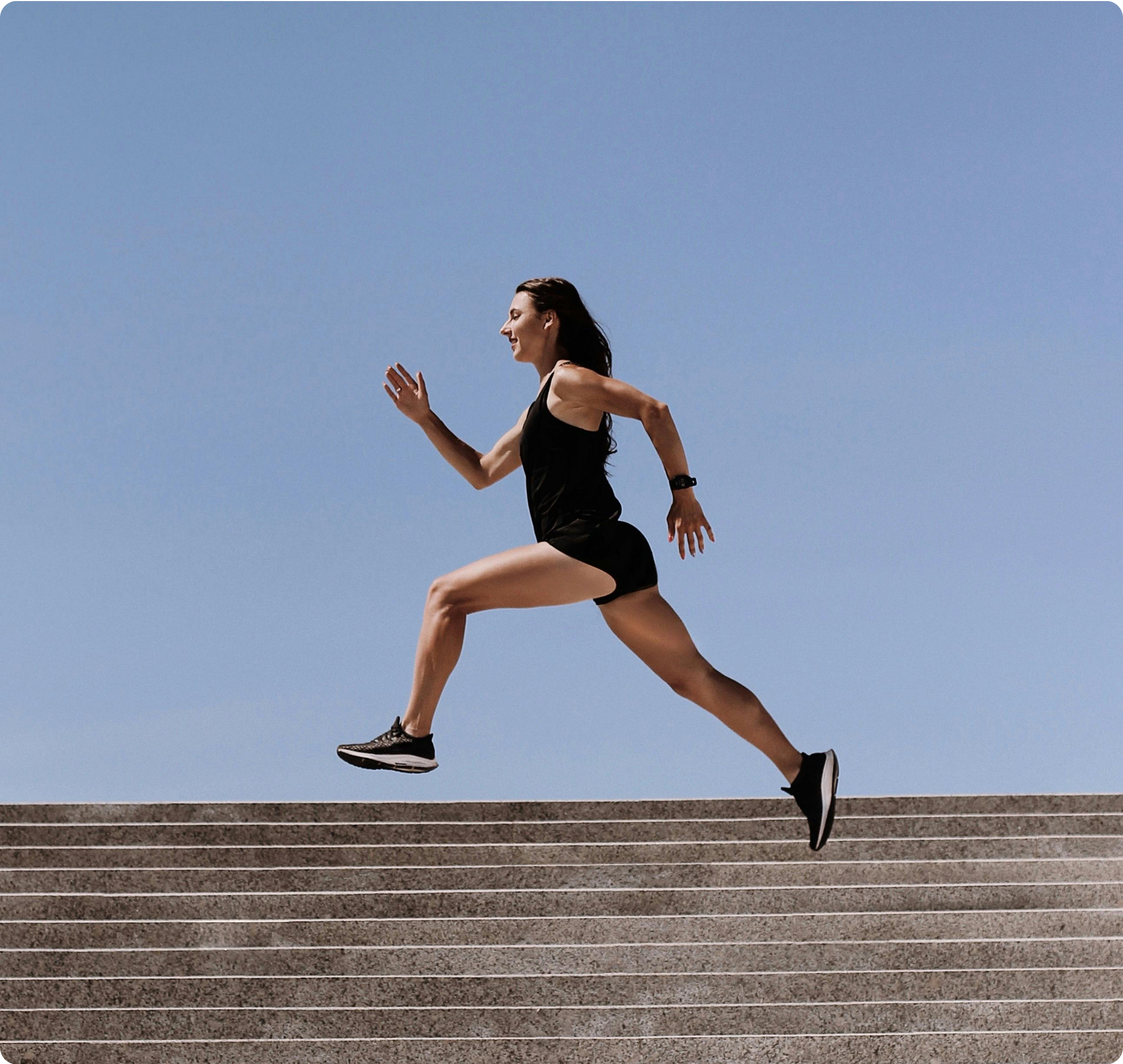 Woman in athletic wear running up concrete steps against a clear blue sky.