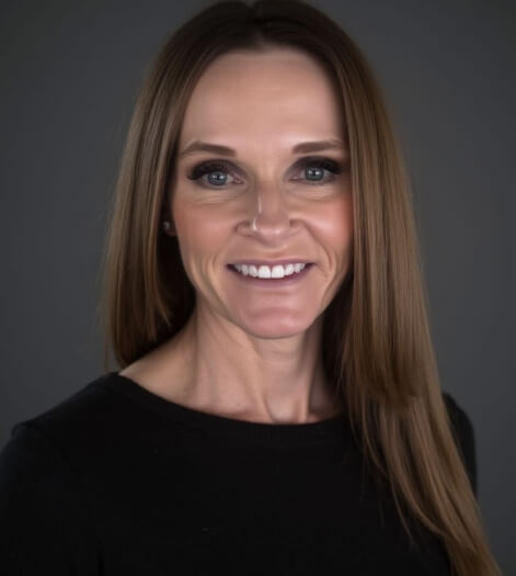 A person with long hair smiling against a gray background.
