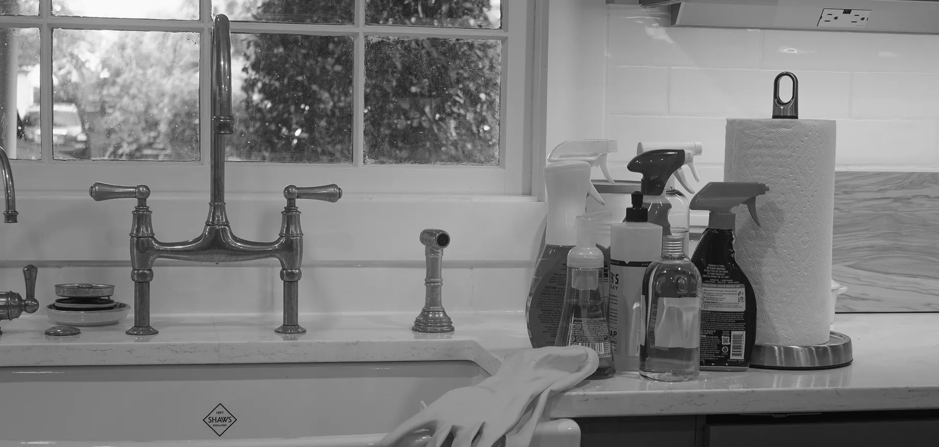 Kitchen sink with faucet, cleaning supplies, and paper towels on the counter.