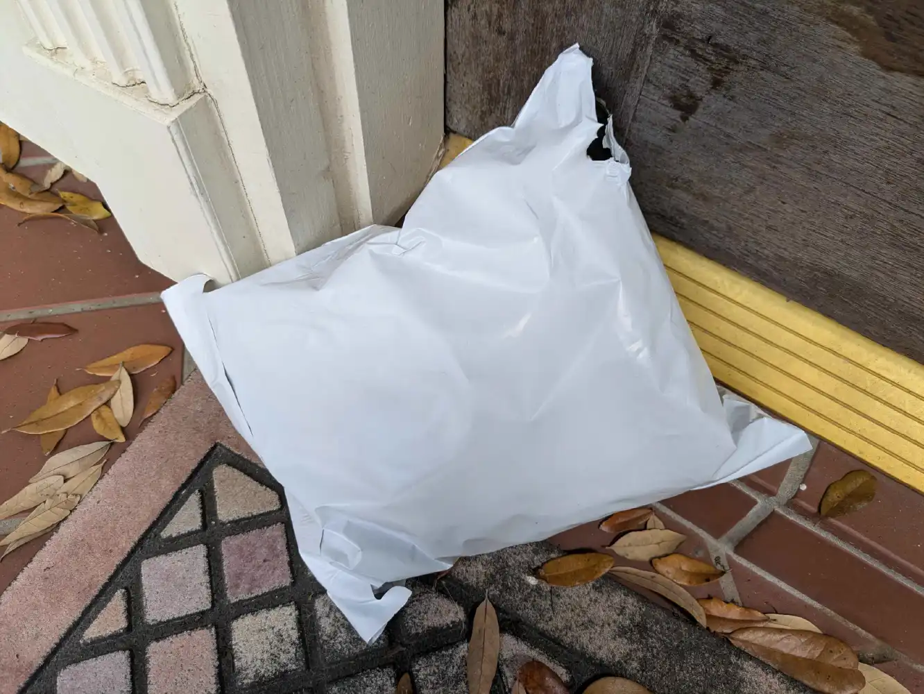 Low quality white poly mailer package delivered to a doorstep damaged
