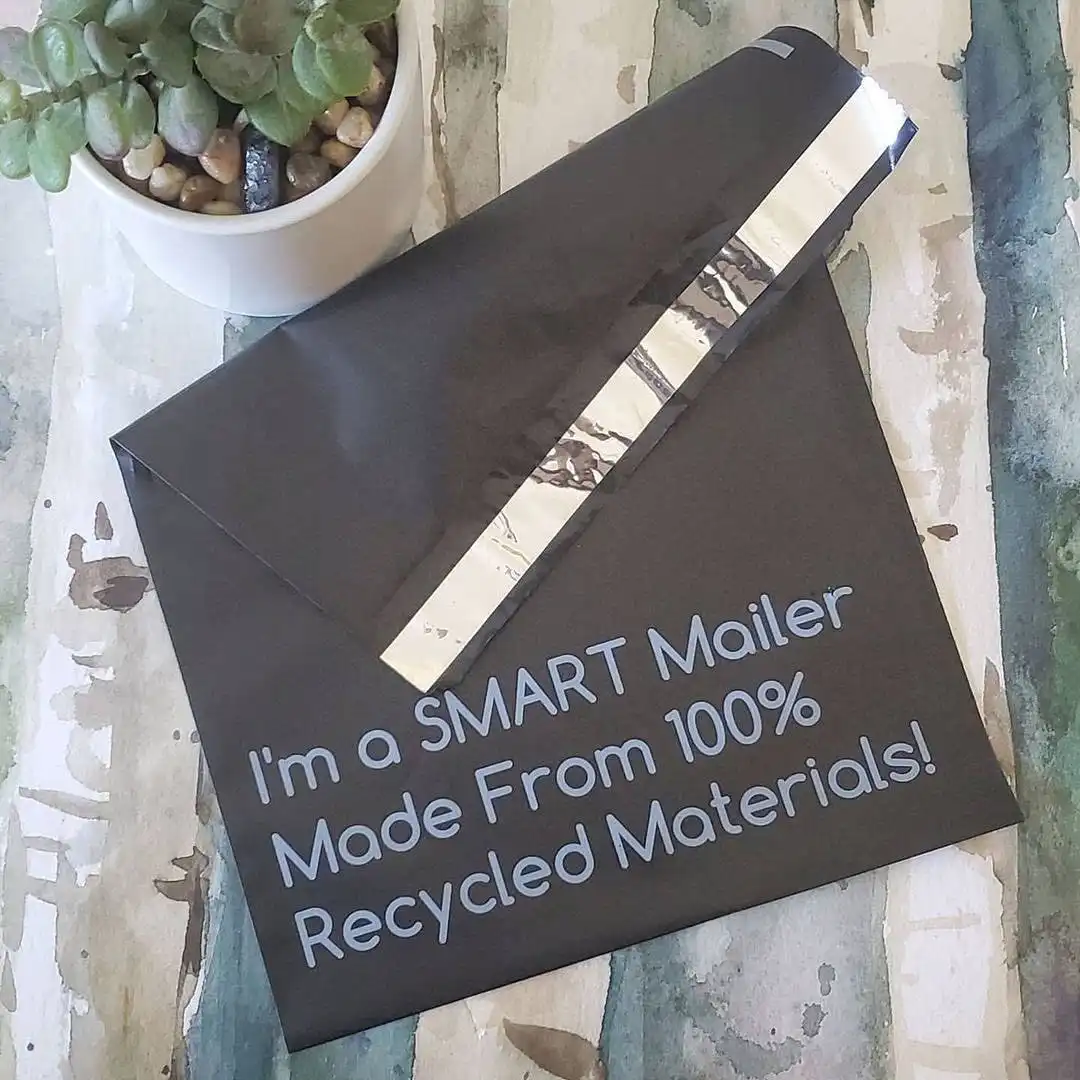 Black poly mailer labeled 'I'm a SMART Mailer made from 100% recycled materials' on a desk with packaging supplies