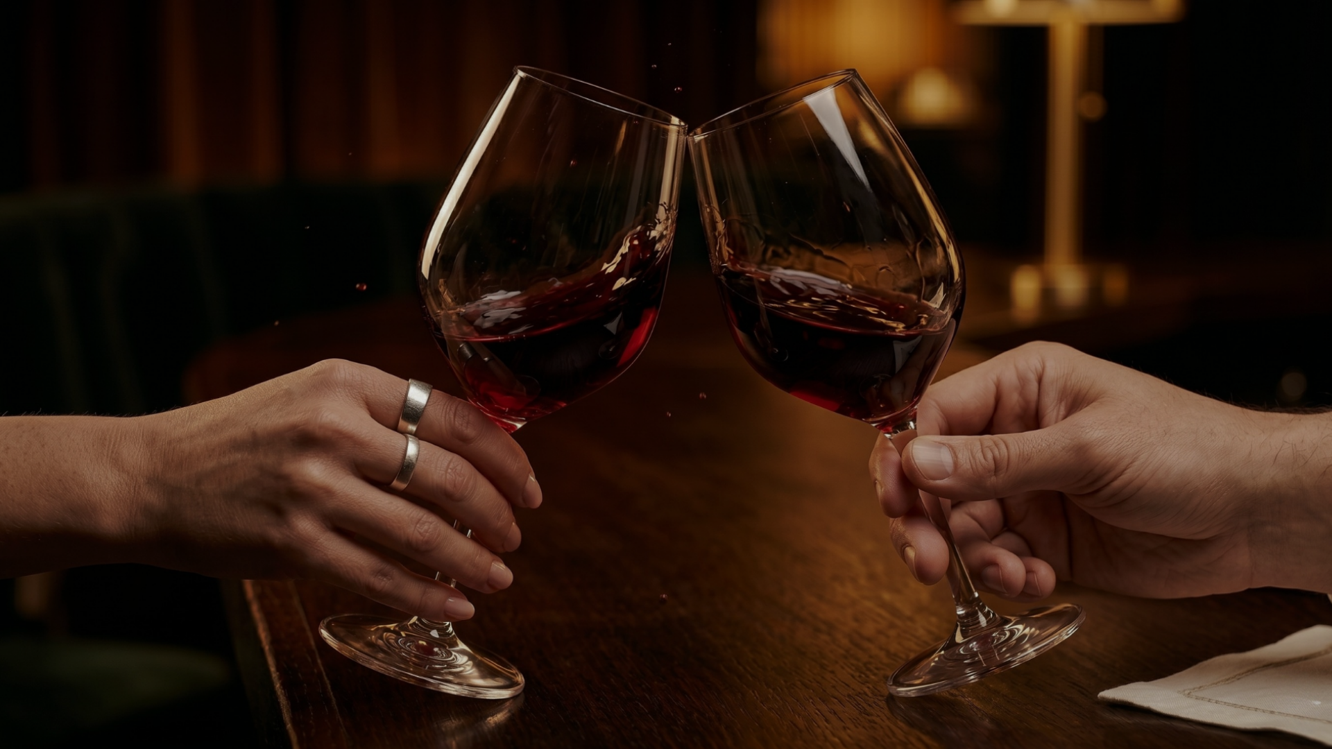 A close-up of two hands clinking glasses of red wine together in a toast.